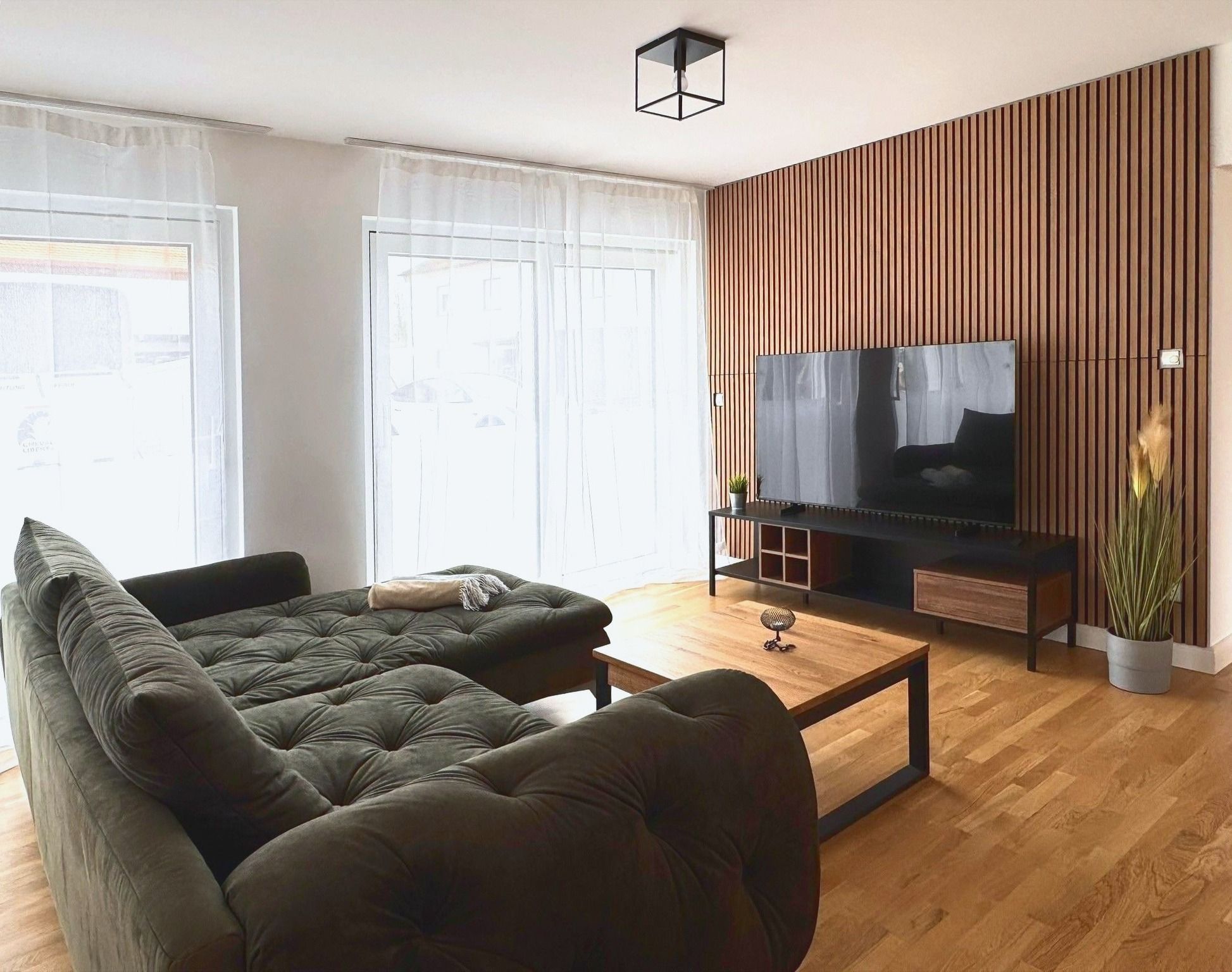 Wohnzimmer mit Ecksofa, Couchtisch und Holzlamellenwand mit Smart TV